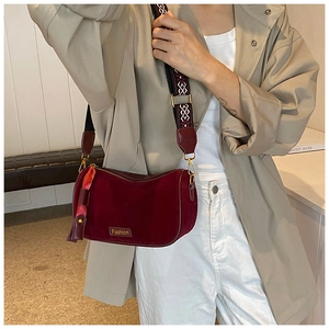 Close-up of velvet pillow bag in burgundy with geometric strap and tassel detail