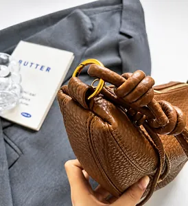Detail of brown litchi pattern leather bag featuring a gold ring and knotted handle