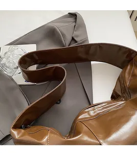 Detail of a brown glossy PU leather hobo bag featuring wide straps and soft texture