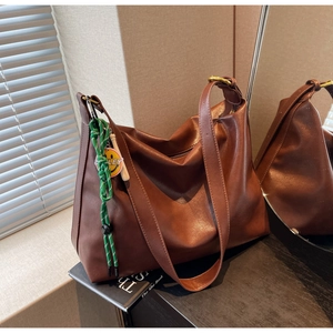 Détail d'un sac cabas marron avec un pendentif nœud vert orné d'un visage souriant