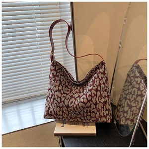 Detailed view of leopard print tote bag with red leather strap and metal logo accent