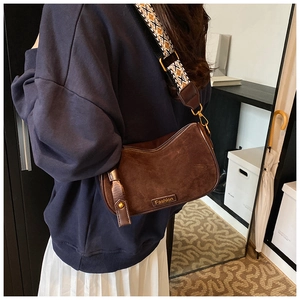 Brown suede crossbody bag with wide patterned ethnic shoulder strap worn by a model