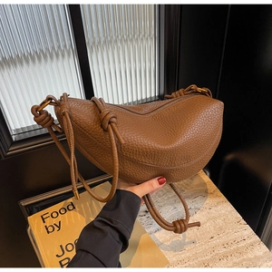 Detailed close-up of brown litchi grain leather texture and knotted strap on half-moon bag