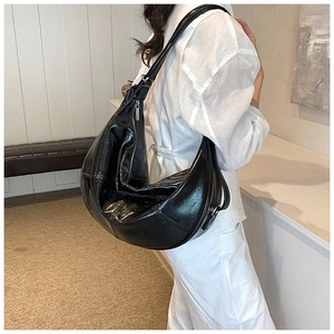 Detail view of large black shiny PU leather hobo bag worn by model in minimalist setting