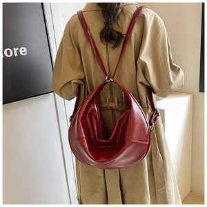 Detail of burgundy glossy patent leather backpack showing stitch texture and metallic rings