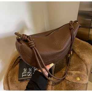 Detail of brown litchi leather bag with decorative knot strap and gold metal hardware