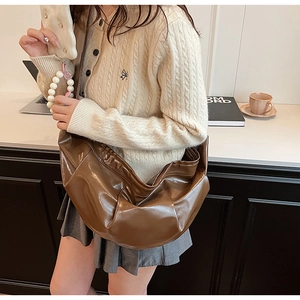 Brown pleated crescent bag with wide strap worn by model in a warm interior setting