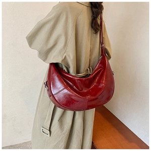 Model wearing a burgundy crescent shoulder bag in glossy oil wax leather finish