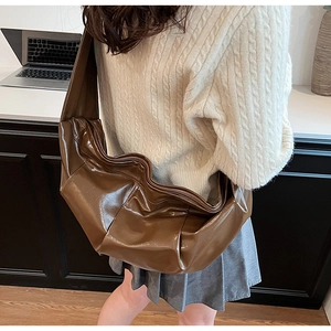 Detail of a large brown pleated crossbody bag with a glossy finish and wide shoulder strap