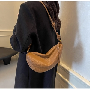 Close-up of caramel brown pebble leather crescent bag with decorative knotted shoulder strap