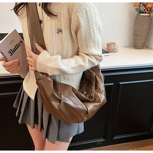 Detail of a brown glossy pleated crescent bag showing premium faux leather texture