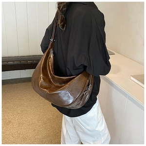 Detailed side view of a large dark brown crescent shoulder bag with glossy leather finish