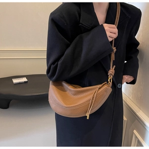 Detailed shot of brown litchi grain leather crescent bag with stylish knotted shoulder strap