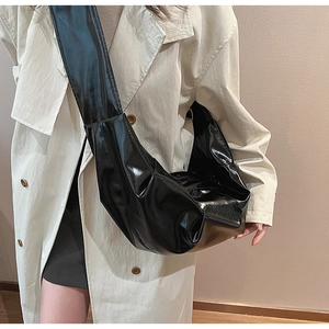 Close-up of black glossy crossbody bag with pleated texture and wide shoulder strap