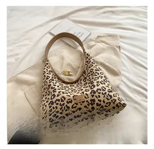 Detail view of leopard print hobo bag featuring brown leather strap and beaded charm