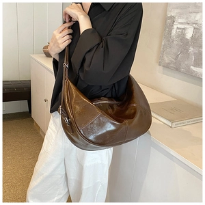 Detail of a deep coffee crescent bag with glossy finish and adjustable shoulder strap