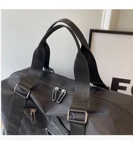 Detail view of black nylon travel bag featuring silver zippers and metallic triangle logo