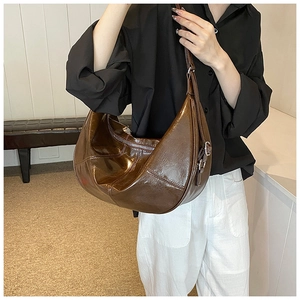 Close-up of caramel brown moon-shaped shoulder bag with adjustable strap and leather texture