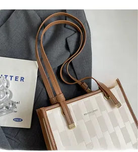 Close-up of woven cream tote bag with brown leather trim and MIKANIOI branding