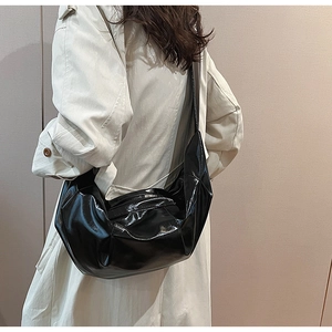 Detailed view of glossy black patent leather crescent bag worn with a light trench coat