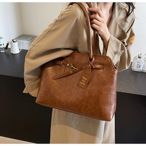 Brown leather tote bag featuring elegant strap details and a metal buckle on a model
