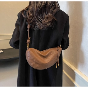 Brown lychee leather crescent bag with knot strap detail worn over a black winter coat