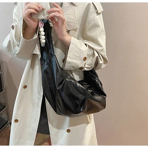 Detail of glossy black pleated dumpling bag with pearl charm and beige coat styling