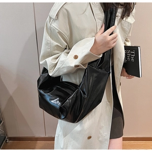 Detail of the black shiny pleated shoulder bag with large capacity on a beige trench coat