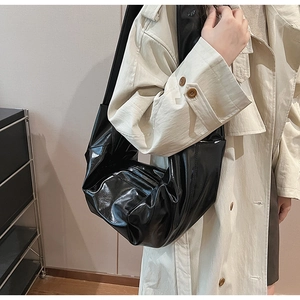 Detail of a black glossy leather slouchy tote bag worn with a beige trench coat