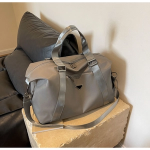 Detailed view of grey nylon travel bag with triangle logo on stone and leather background