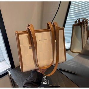 Detail of a contrast woven tote bag with brown straps on a black wooden side table
