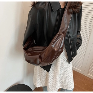 Detail of a large dark brown pleated leather crescent bag worn by a model in a casual setting