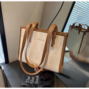 Detail of a structured beige tote bag with brown handles and woven texture on the surface
