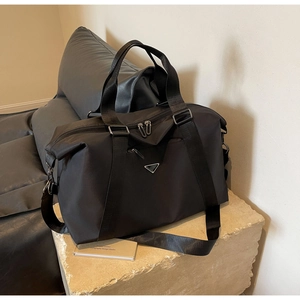 Detail of a large black nylon travel bag with a metal triangular plaque on a stone base