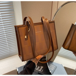 Detail of brown tote bag showing geometric texture, silver hardware and brand logo