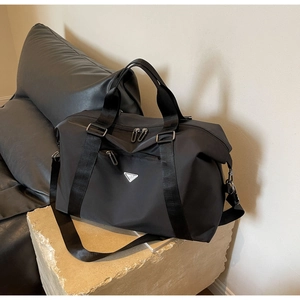 Detail of black large capacity travel bag with metal triangle logo on stone base