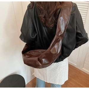 Detail of dark brown glossy croissant bag showing high shine texture and wide strap