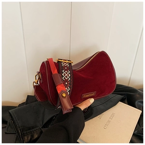 Detail of burgundy velvet cylinder bag with embroidered vintage geometric strap and logo tag
