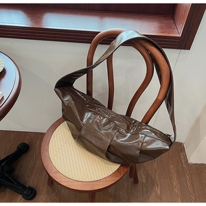 Detail of a brown pleated crescent bag with glossy PU leather finish on a wooden chair