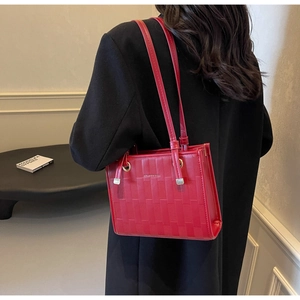 Red woven texture tote bag with thin straps and gold hardware styled on a black wool coat