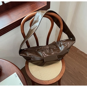 Detail view of large dark brown dumpling bag with pleated glossy leather on wooden chair