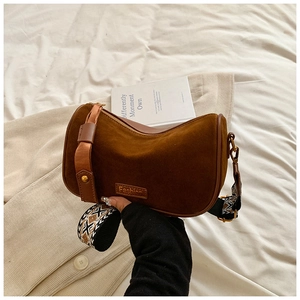 Detail of brown suede half-moon bag featuring ethnic wide strap and fashion leather tag