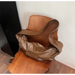 Detail of a brown pleated dumpling tote bag showing soft leather texture on a wooden chair