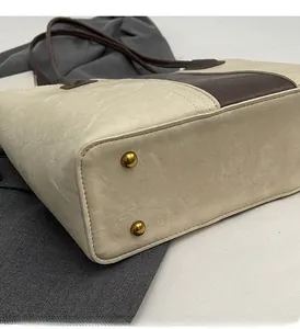 Detail view of the bag's bottom with golden metal studs and white pebble leather