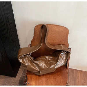 Brown high-gloss leather tote bag with thick strap placed on a vintage wooden chair