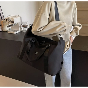 Detail of a large black nylon travel bag with dual handles and metal triangle plaque