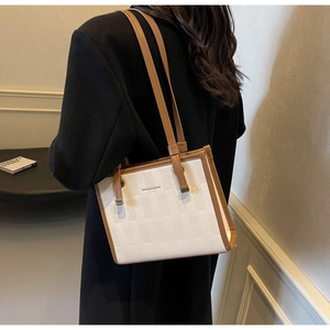 Detail of large tote bag showing cream woven texture and brown leather trim accents