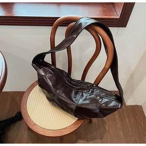 Detailed view of deep brown crescent shoulder bag made of shiny leather on wooden chair