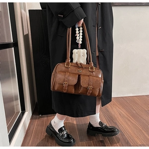 Brown leather shoulder bag with dual front pockets shown on a model in a minimalist setting