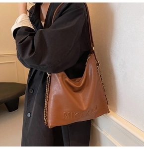 Dettaglio della borsa tote in pelle marrone con scritte in rilievo e tracolla a catena